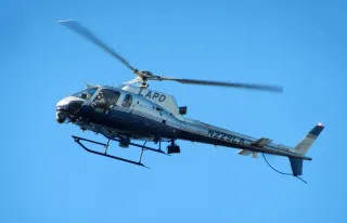 A blue and silver helicopter in flight emblazoned with the letters LAPD beneath its spoke