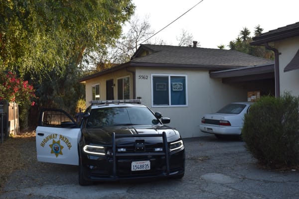 A California Highway Patrol car is parked outside of a brown house.